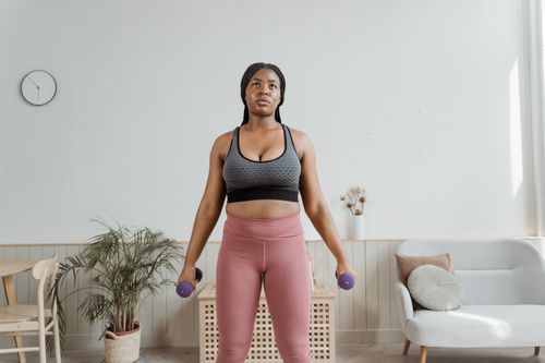 Free A woman in activewear exercises with dumbbells in a cozy home setting. Stock Photo