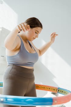 Woman in activewear hula hooping indoors, embracing fitness and healthy living.