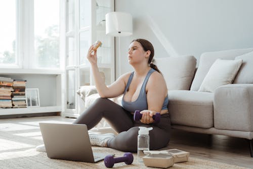 Woman Staring at a Donut while Holding a Dumbbell