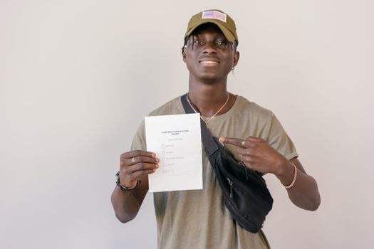 Young adult smiling and pointing at electoral ballot paper, emphasizing the importance of voting.