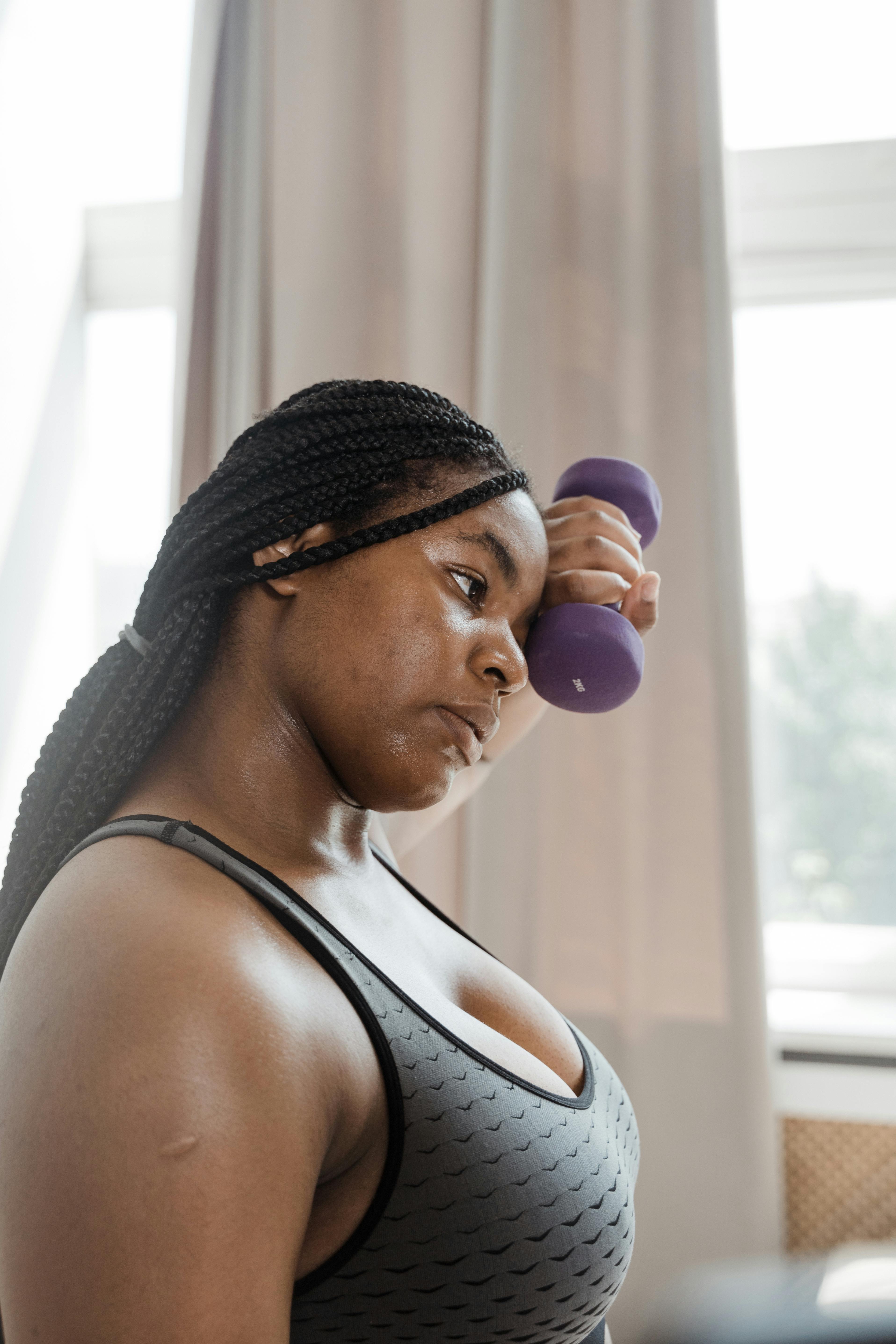 A confident Black woman with braided hair lifting weights indoors, embracing body positivity.