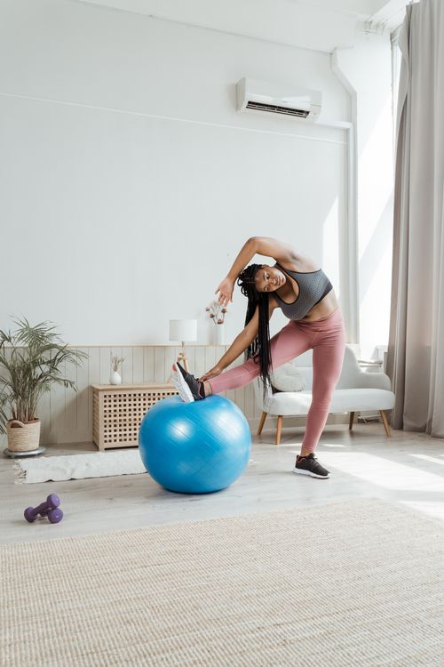 Free A woman in activewear stretches with a yoga ball in a bright and airy living room. Stock Photo