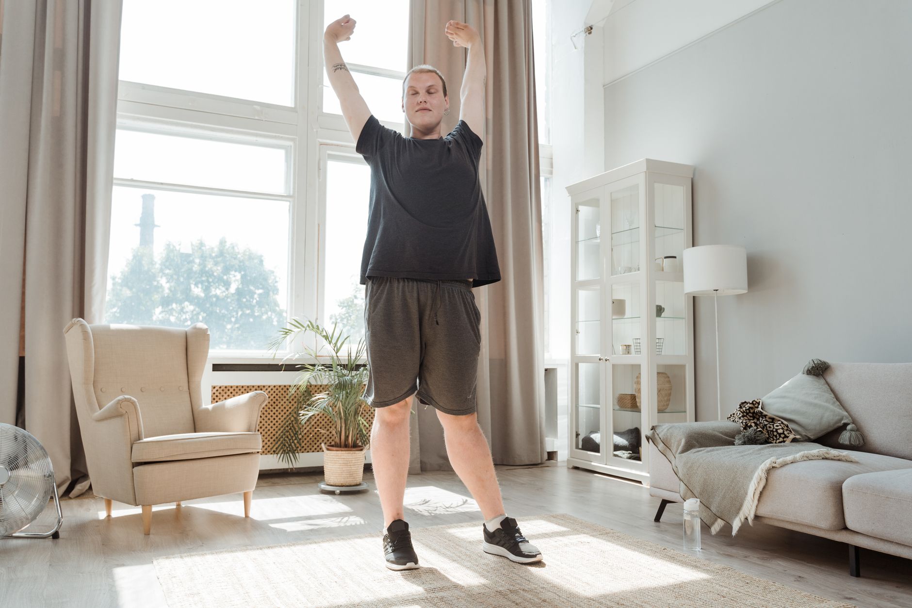 你也可以做到!簡單健身方法:輕鬆融入日常 A young man enjoying a morning stretch in a bright, airy living room, embracing a healthy lifestyle.
