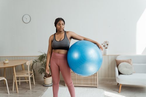 Free Woman in activewear holding an exercise ball indoors, promoting fitness and wellness. Stock Photo