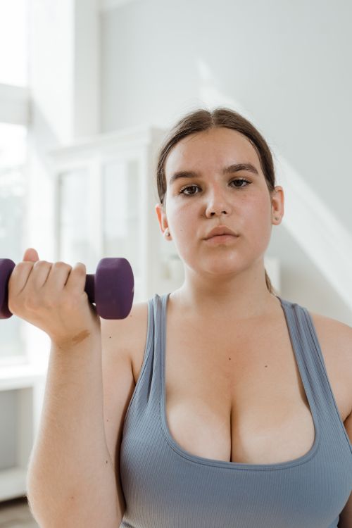 Free Plus size woman in sports bra lifting a dumbbell indoors, showcasing strength and confidence. Stock Photo
