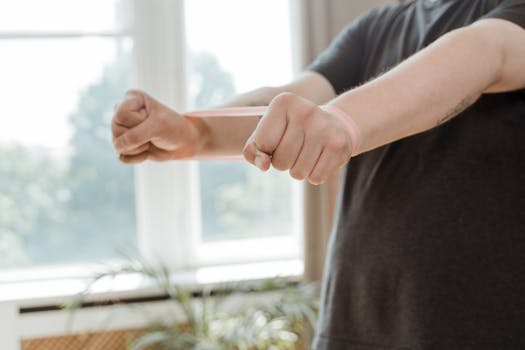 A man uses a resistance band for arm exercises in a bright indoor setting.