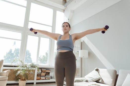 Determined young woman in activewear lifting dumbbells indoors for fitness.