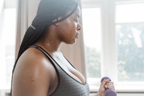 Free Side view of a focused African American woman working out with a dumbbell indoors. Stock Photo