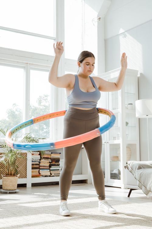 Free Woman enjoying fitness exercise indoors with colorful hula hoop showcasing healthy lifestyle. Stock Photo