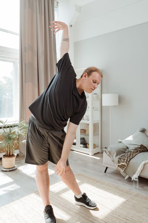 Free Young man stretching indoors, promoting exercise and a healthy lifestyle. Bright and inviting setting. Stock Photo