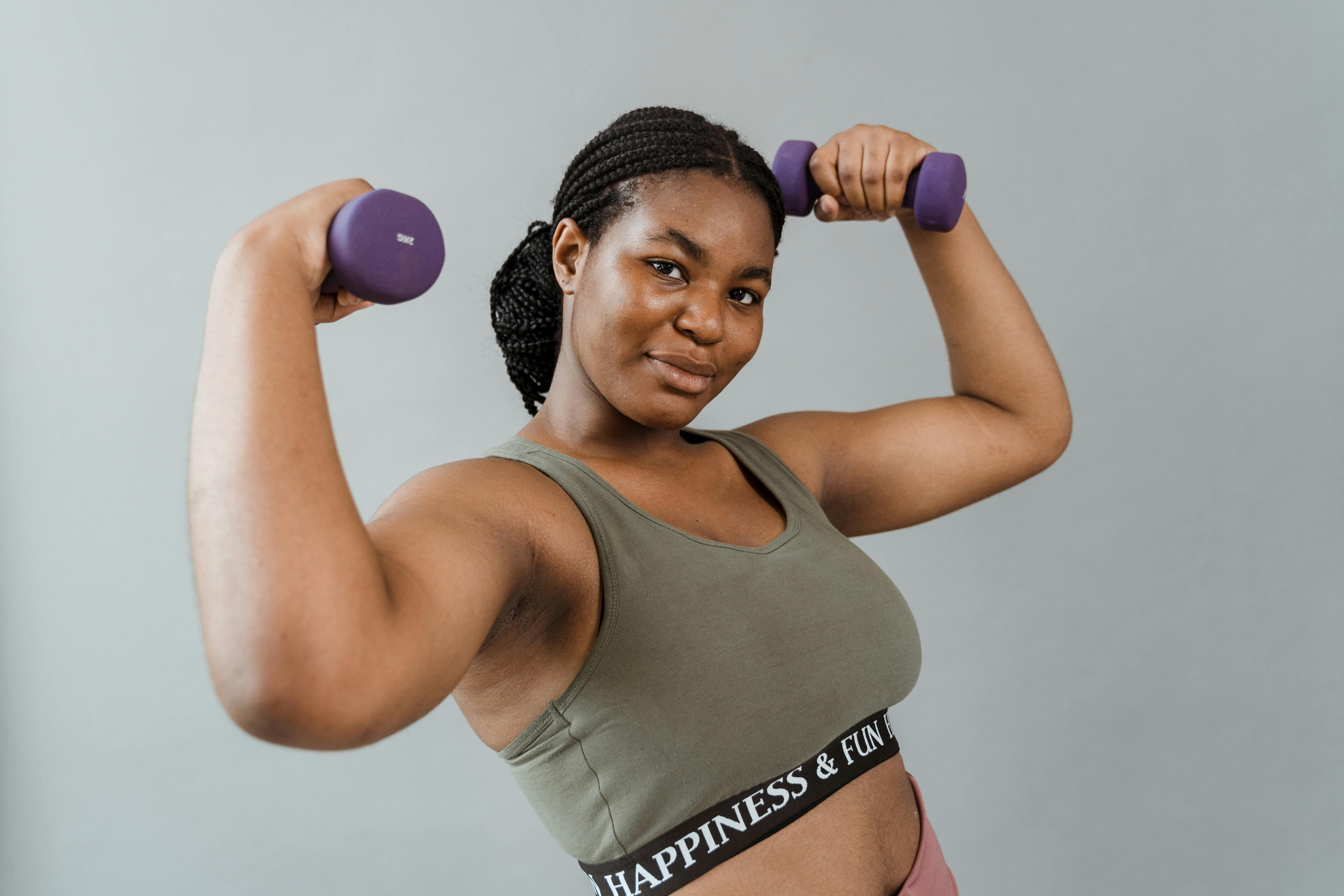 Black woman doing bicep curl with dumbbell at gym