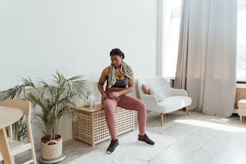 Free Woman in Black Sports Bra and Pink Leggings Sitting on Wooden Table Stock Photo
