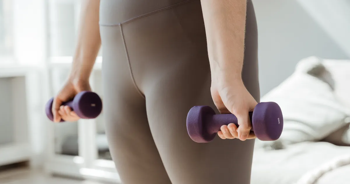 Someone holding a light pair of dumbbells by their sides at home