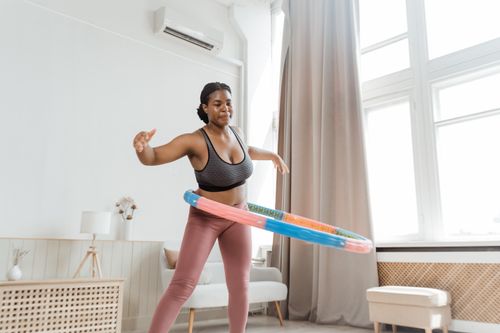 Free Black woman hula hooping at home, showcasing indoor fitness and health. Stock Photo