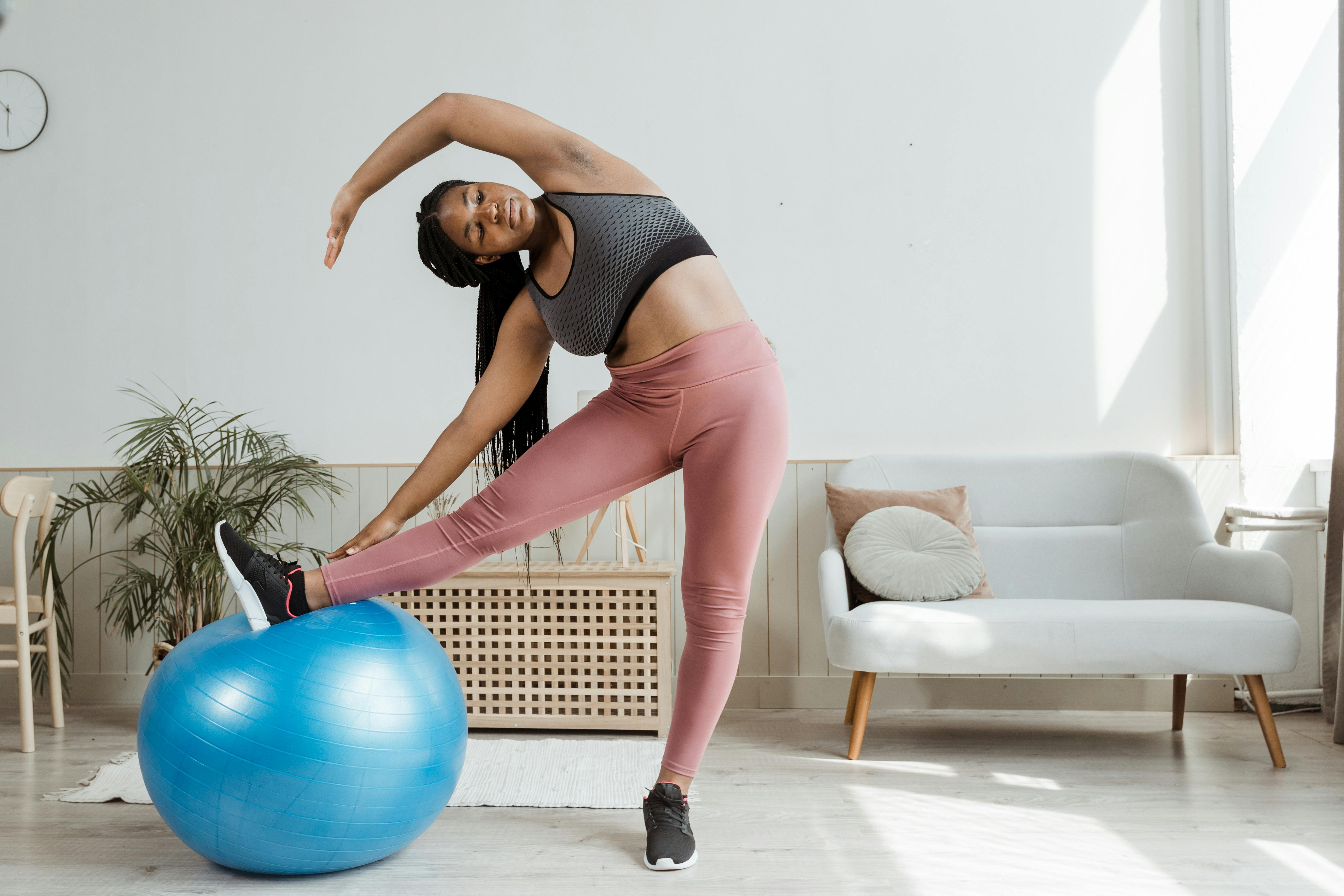 Woman in Black Sports Bra and Pink Leggings Doing Arms and Legs Stretching  Using a Blue Gym Ball · Free Stock Photo