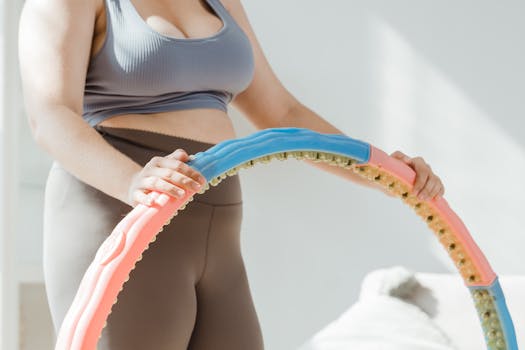 A woman wearing activewear exercises indoors with a colorful hula hoop.