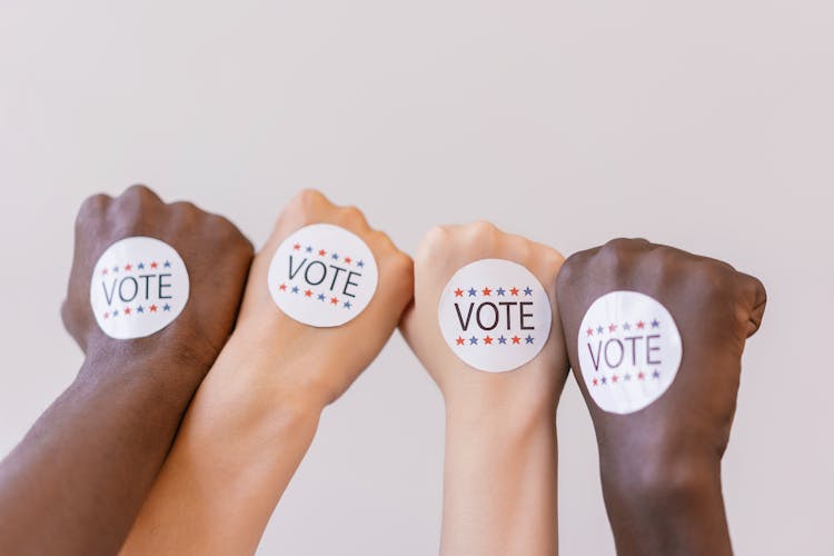 Close Up Photo Of Vote Stickers On People's Fist