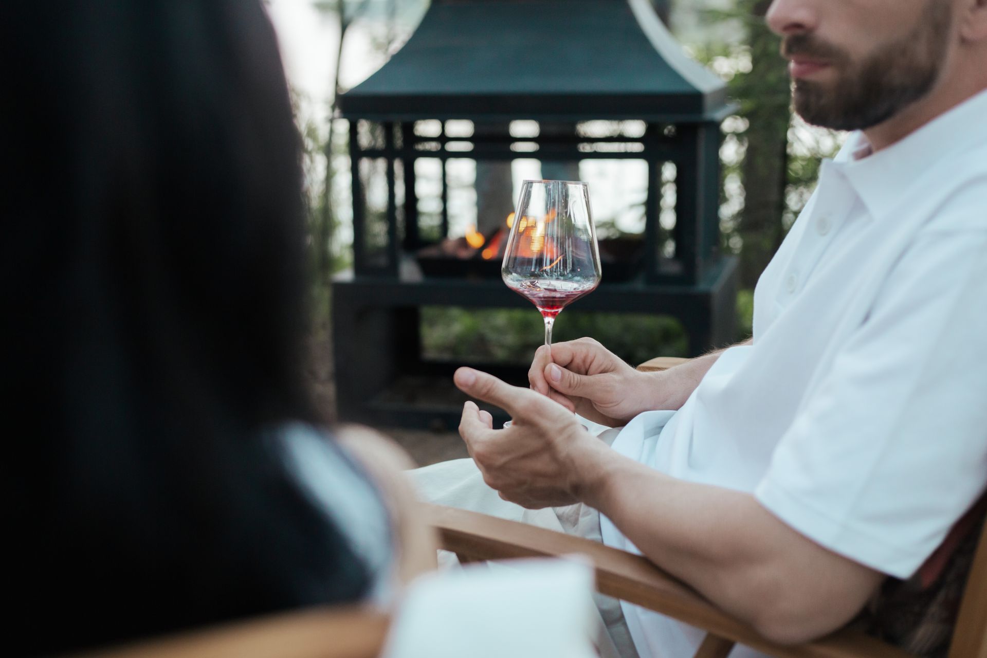 A person enjoys a glass of wine by the fireplace outdoors, creating a cozy ambiance.