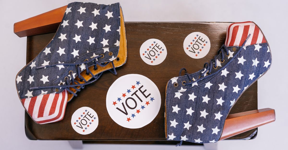 High heel shoes with stars and stripes, surrounded by voting campaign stickers on a wooden surface.