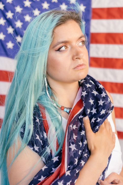 Free Close-up of a woman with blue hair holding an American flag, expressing patriotism. Stock Photo