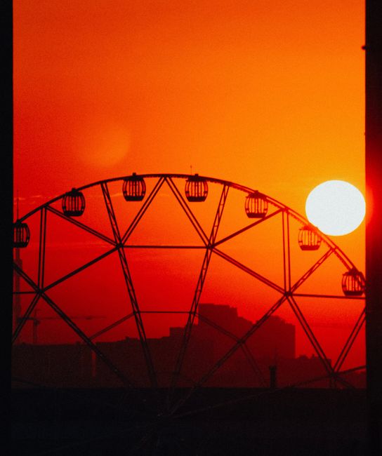 A striking silhouette of a Ferris wheel against a vibrant orange sunset sky.