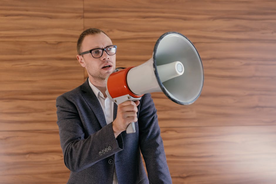 Man in suit holding a megaphone, making a public announcement indoors.