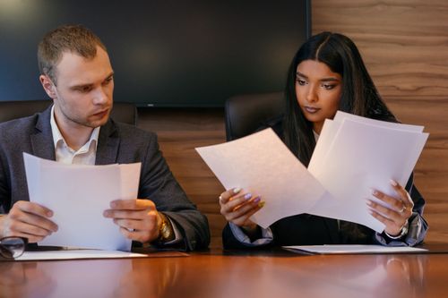 Free Two diverse professionals reviewing documents in a modern office setting, showcasing teamwork and focus. Stock Photo