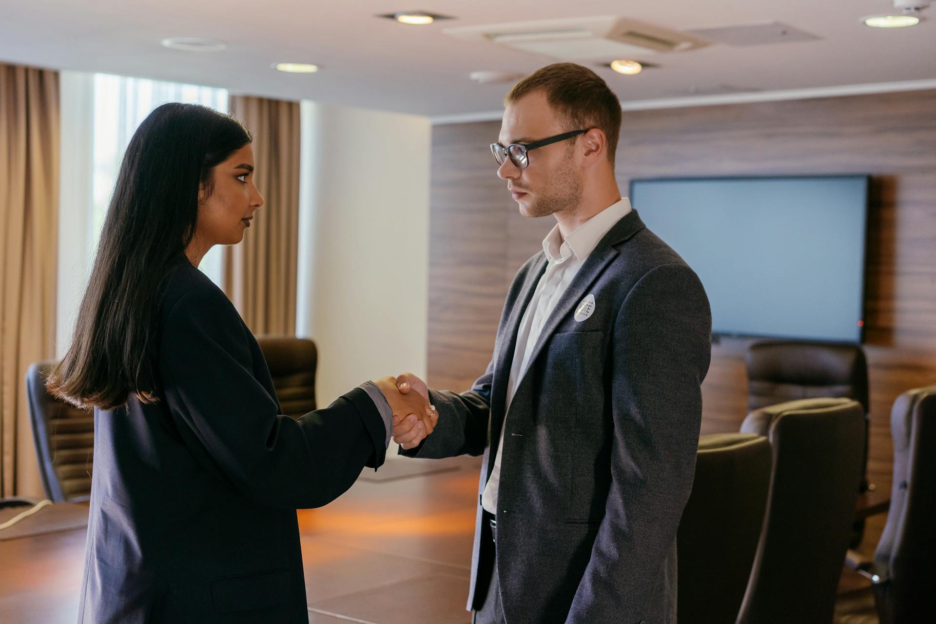 Two professionals shaking hands in a modern conference room, symbolizing successful business agreement.