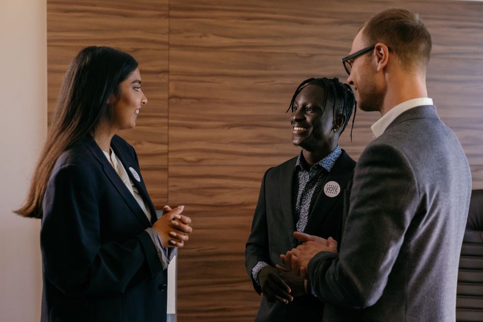 Three professionals engaged in conversation within a modern conference room setting.