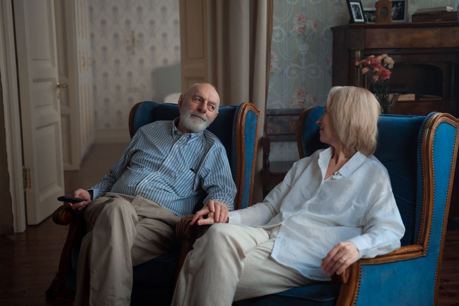 Older couple sitting close together and holding hands in their living room