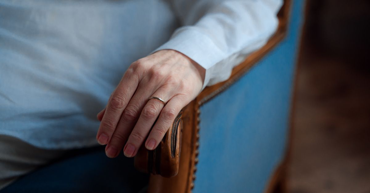 Gros plan sur une main avec une alliance reposant sur un fauteuil bleu, capturant élégance et simplicité.