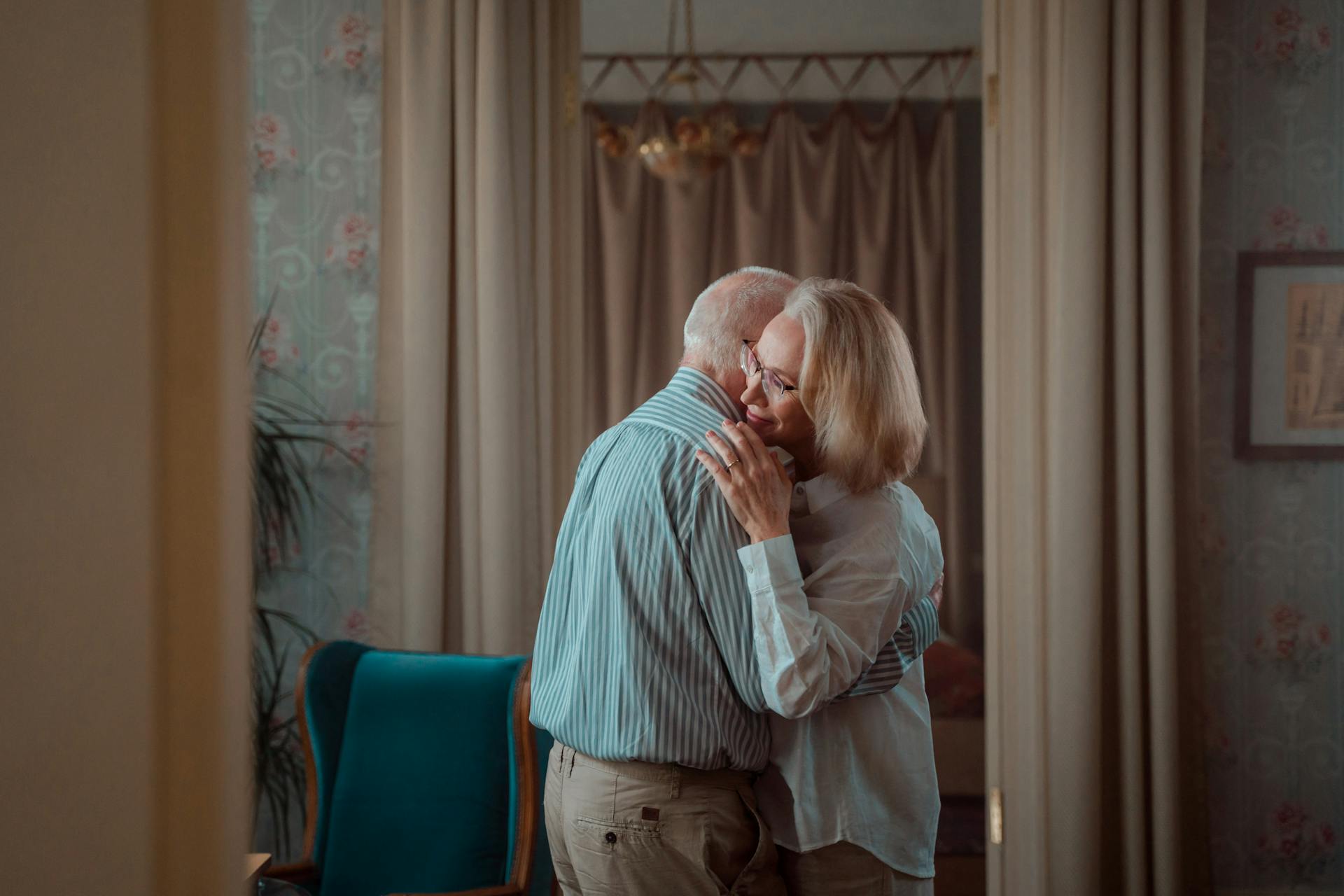 An elderly couple shares a tender embrace in a comfortable home setting, symbolizing lasting love and companionship.