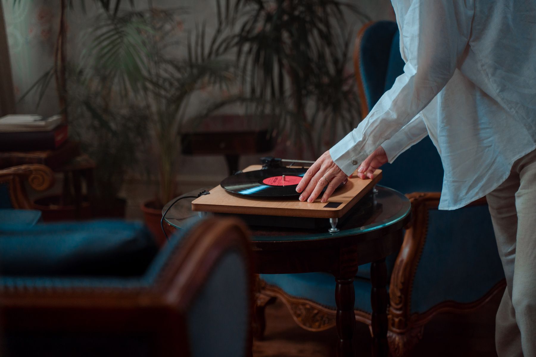 Hands lowering a vinyl record onto a turntable on a wooden table