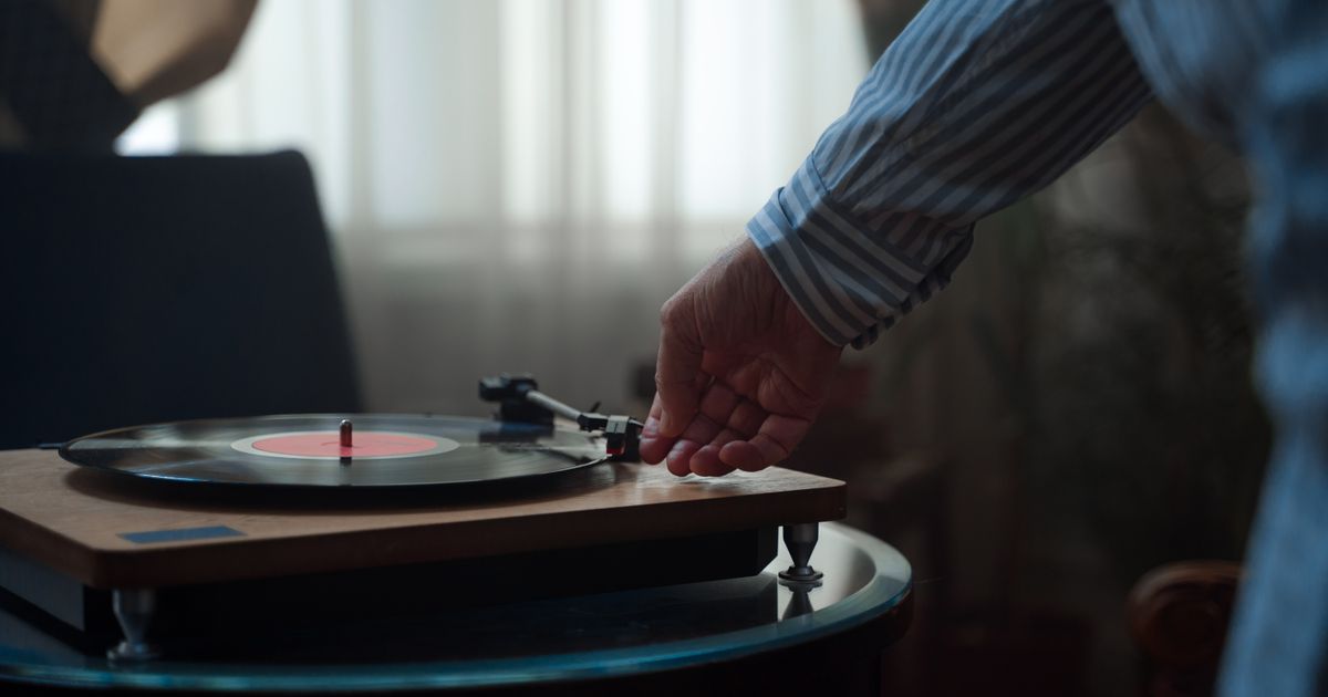 A hand adjusting the needle on a vintage turntable playing a vinyl record indoors.