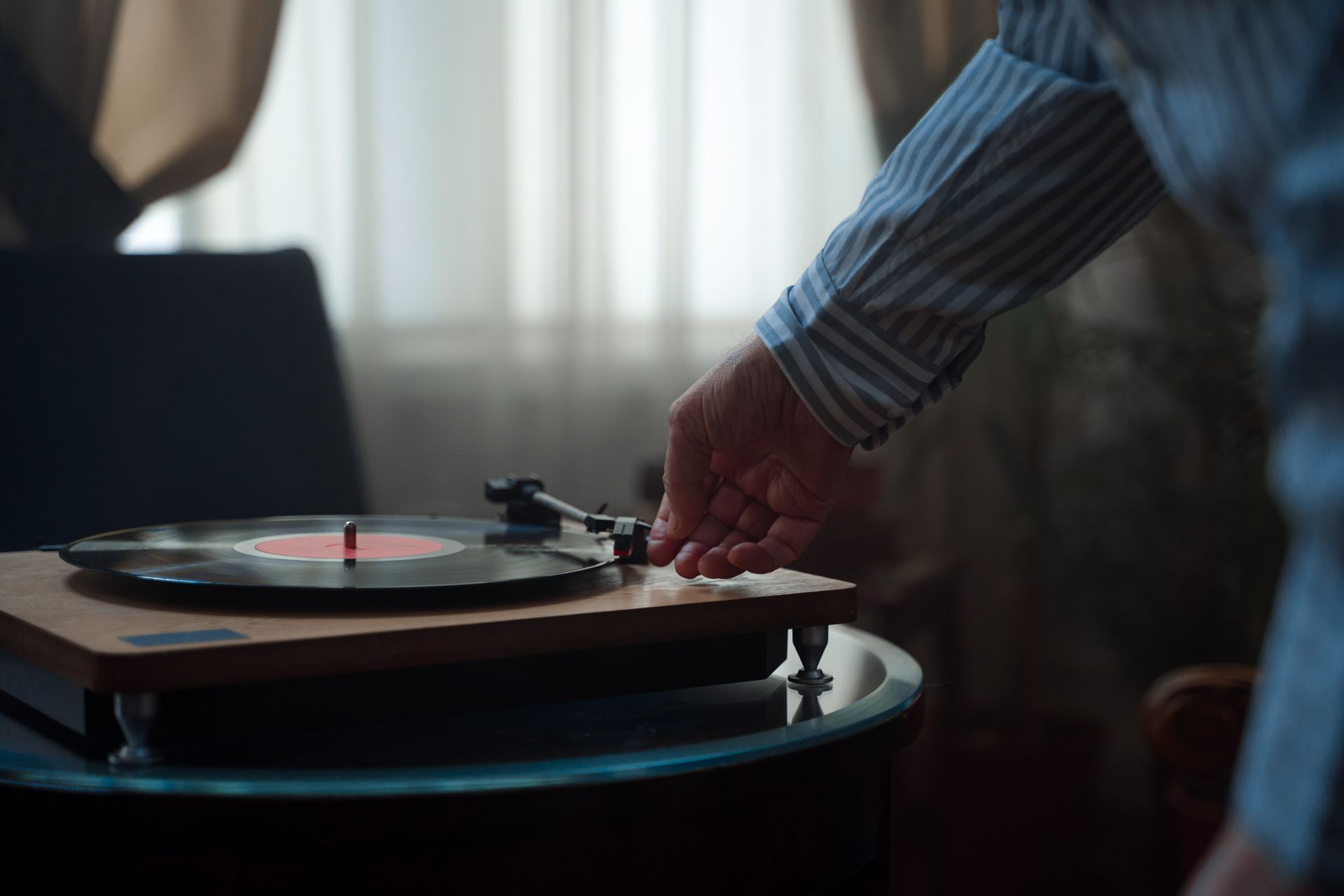A hand adjusting the needle on a vintage turntable playing a vinyl record indoors.
