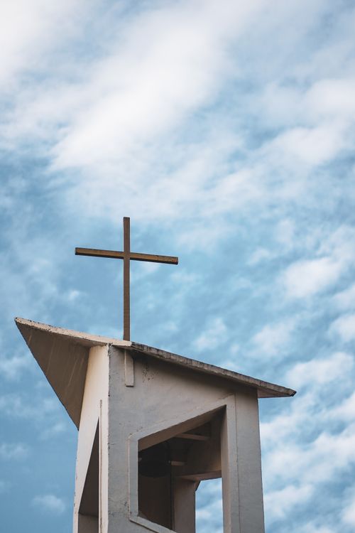 Free Low angle view of a cross on a church tower with a bright blue sky and clouds in the background. Stock Photo