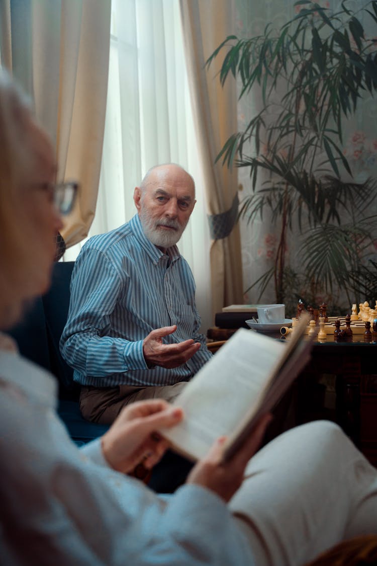 Elderly Man Looking At His Wife Reading A Book