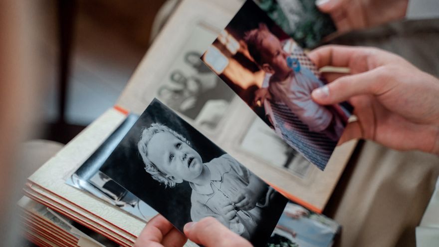 A pair of hands looking through old family photographs in an album, representing the reflective work of examining your maternal and paternal ancestral lines