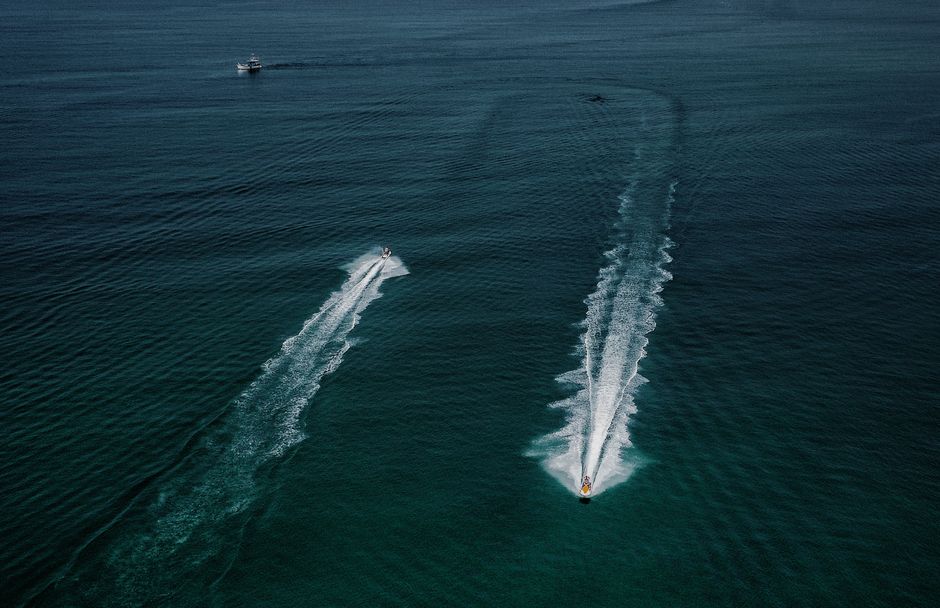 Dynamic aerial shot capturing motorboats racing across the ocean, leaving trails on the water surface.