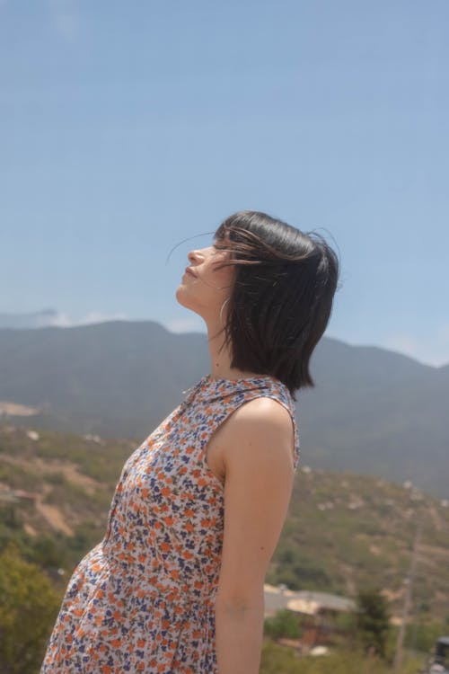 Woman in a Floral Dress Standing with her Face Towards the Sun 