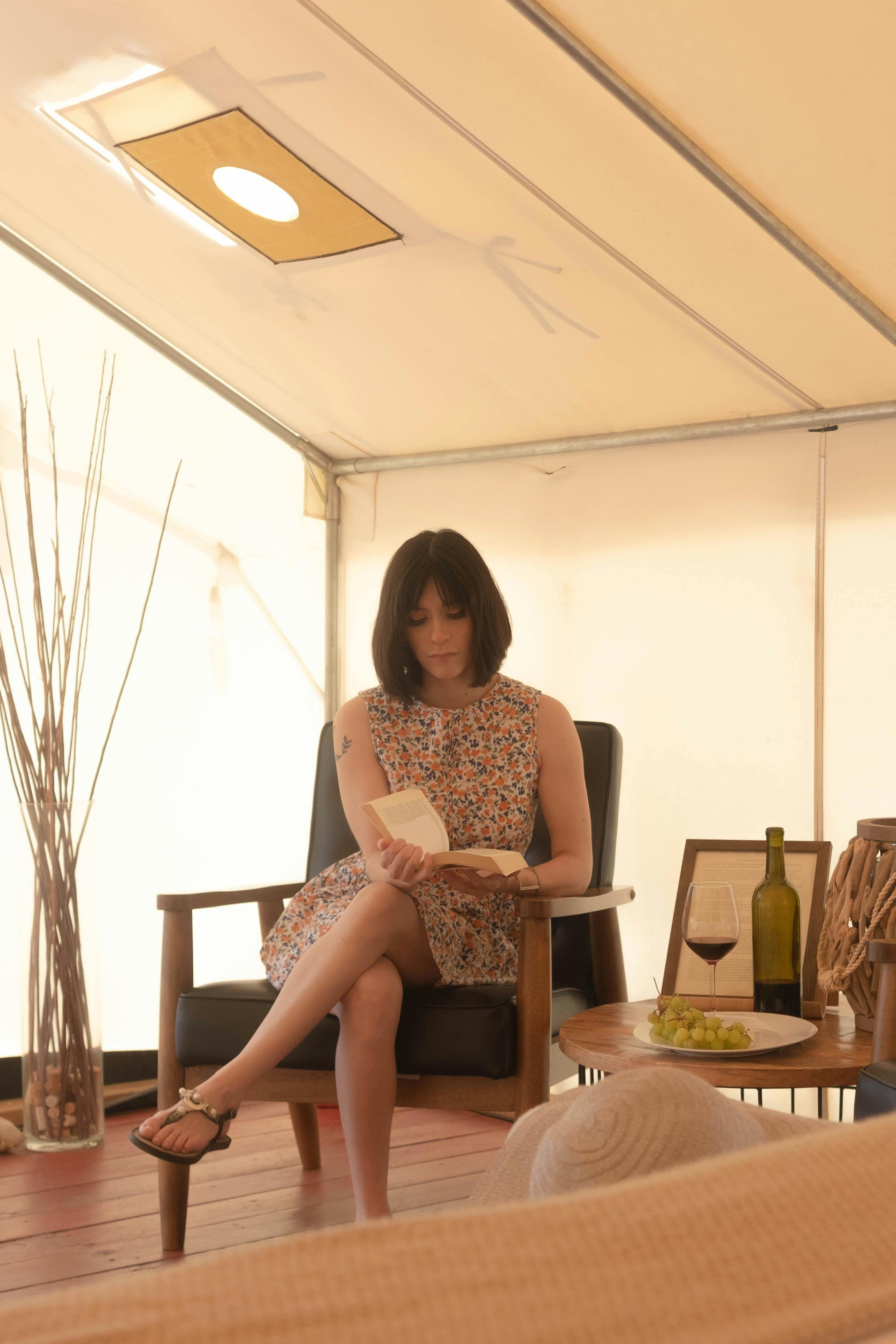 woman in floral dress sitting on brown armchair reading a book