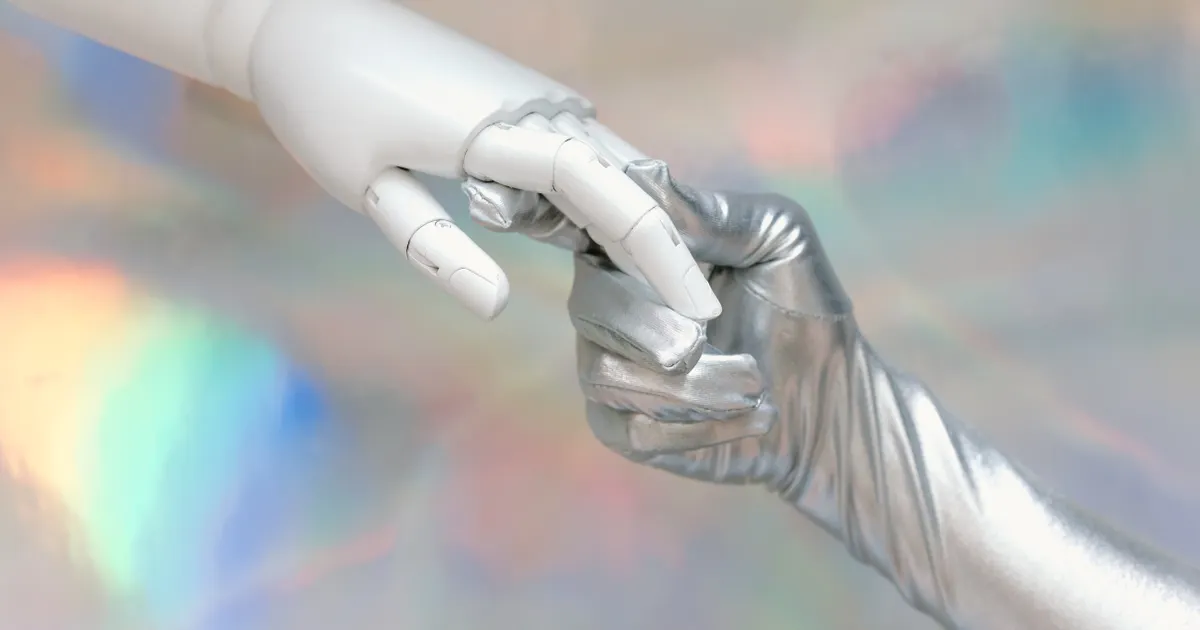 A white robotic hand touching a silver-gloved hand, representing ISO 42001 Section 5.3 requires documented role assignments for the AI management system representative