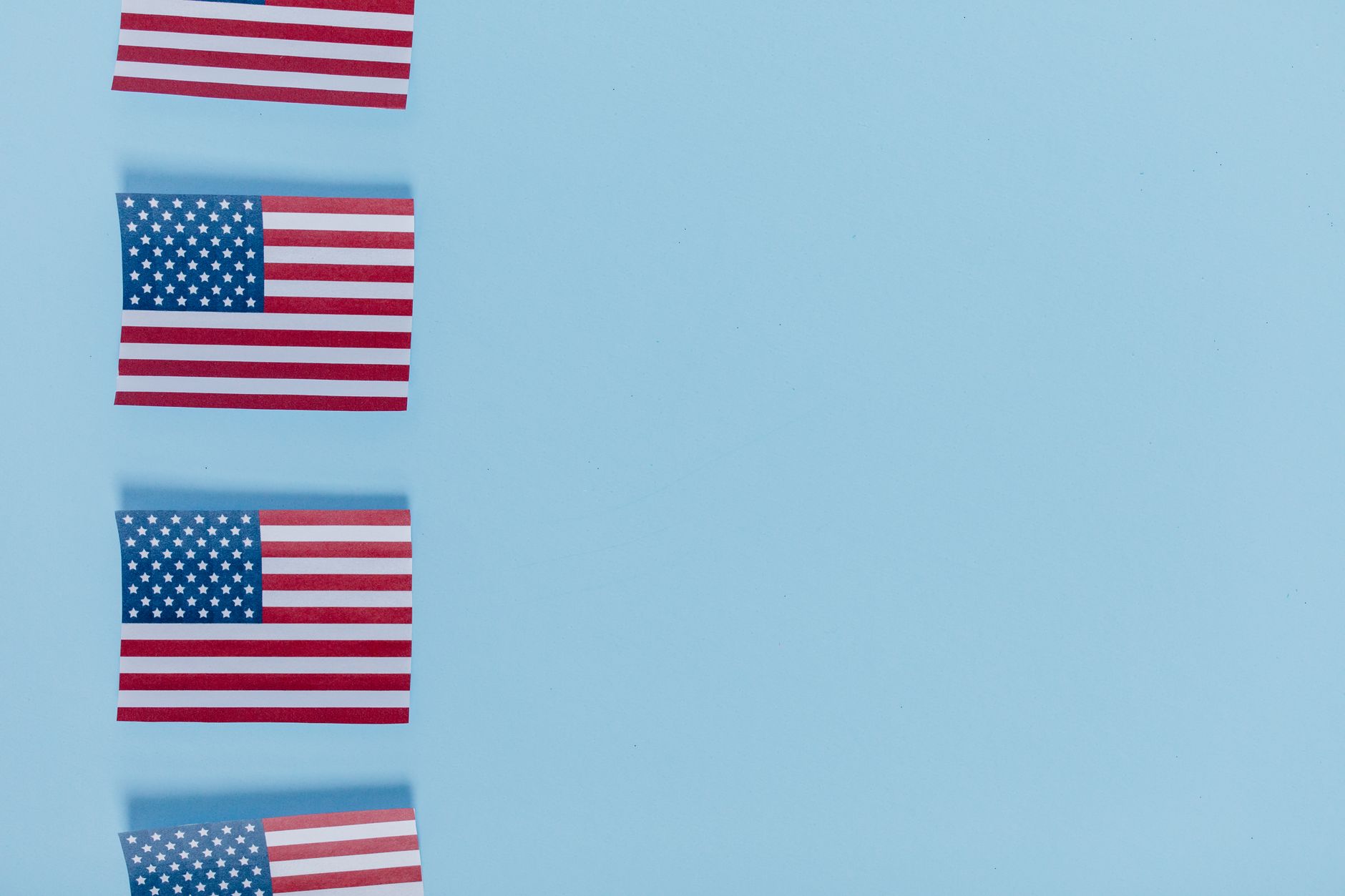Four American flags aligned on a light blue background with copy space.