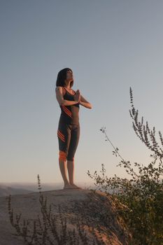 A woman meditating in a yoga pose on a rock during sunset, embracing nature.