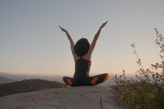 A woman doing yoga outdoors on a rock at sunset, embodying relaxation and mindfulness.