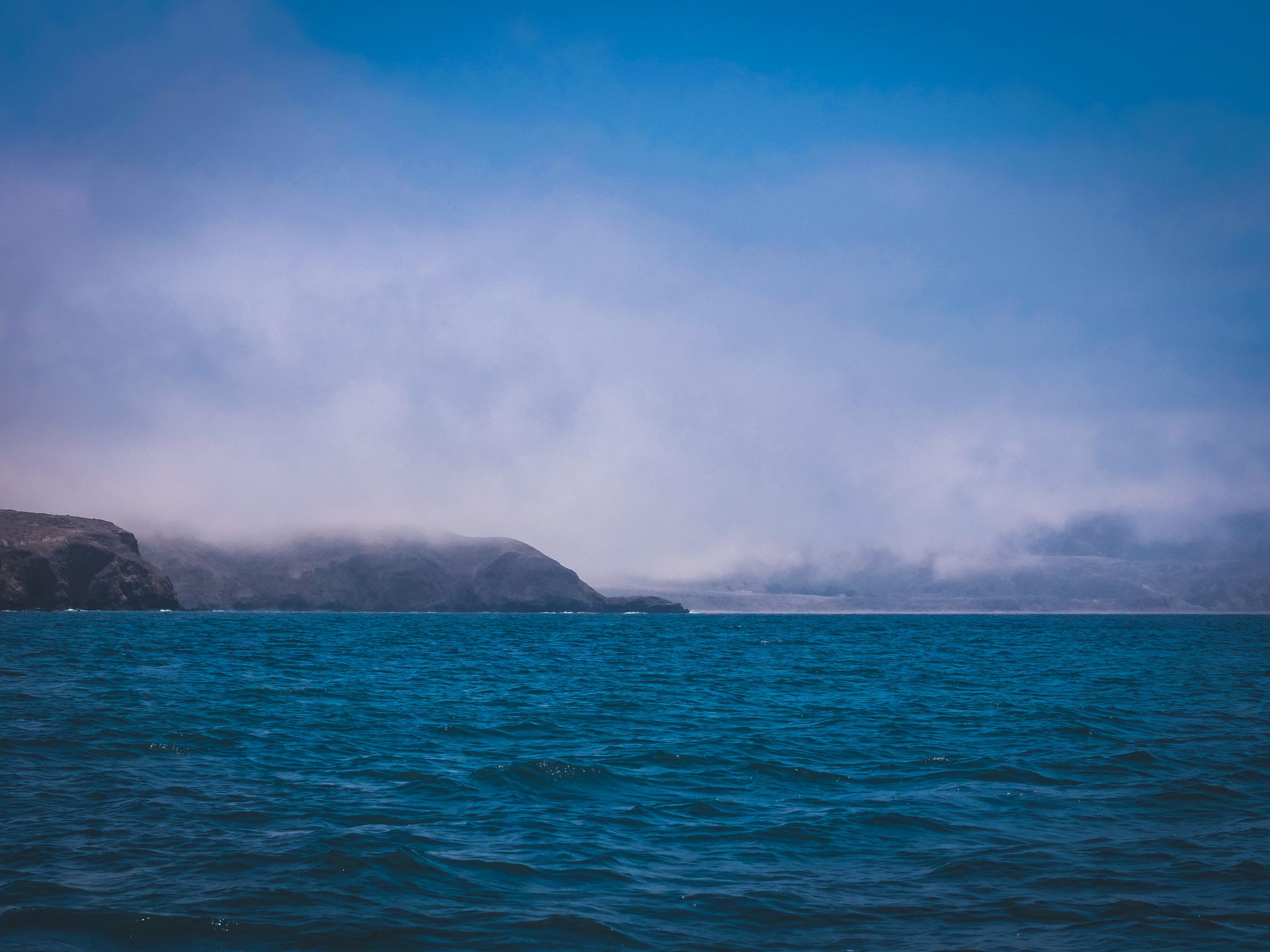 A serene view of a misty ocean landscape with a rocky island in the distance under a blue sky.