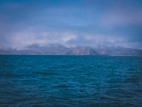 Stunning seascape featuring a blue ocean with misty coastal mountains in the distance.
