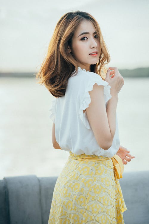 Foto De Mulher Vestindo Camisa Branca Sem Mangas E Saia Floral Amarela Perto Da água