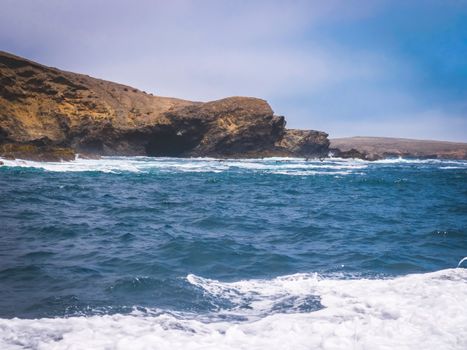 Majestic coastal cliff scenery with vibrant blue waves crashing against rugged cliffs under clear skies.