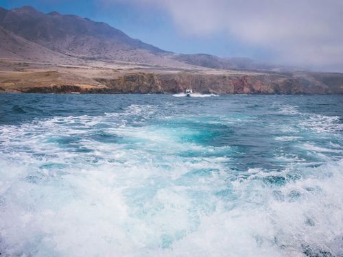 Free A distant boat navigating through turquoise ocean waves near rocky coastline. Stock Photo